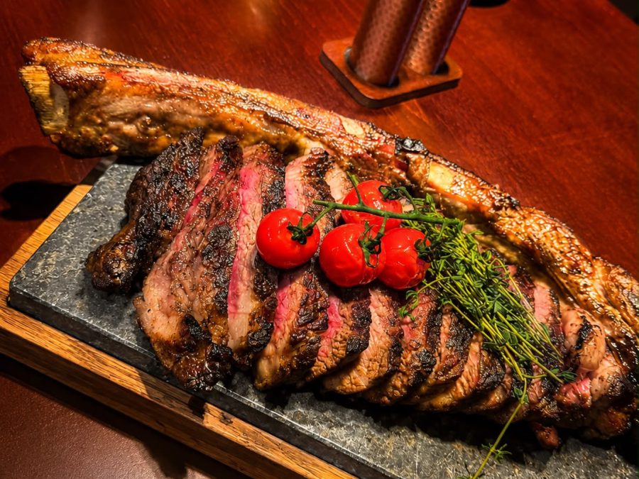 Aufgeschnittenes Steak am Knochen mit Ofentomaten auf heißem Stein